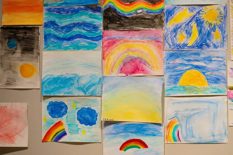 A wall of children's paintings showing sunrises, rainbows and open horizons