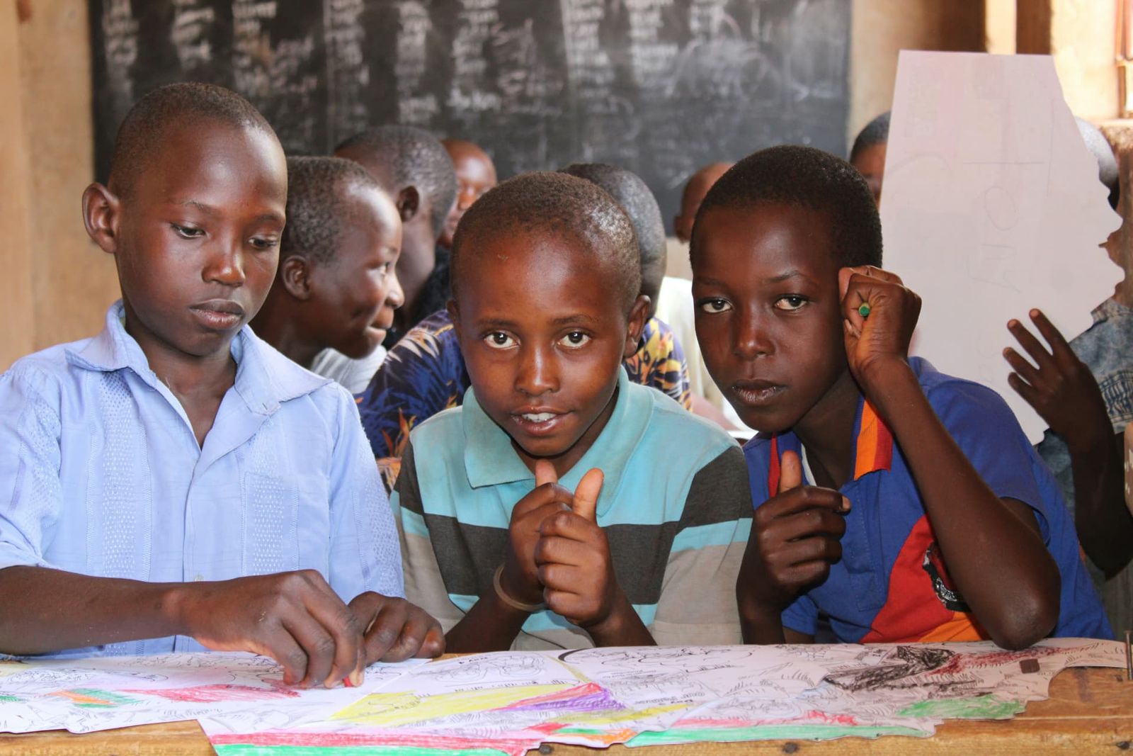 Schoolchildren working on drawings at a shared desk in front of a blackboard