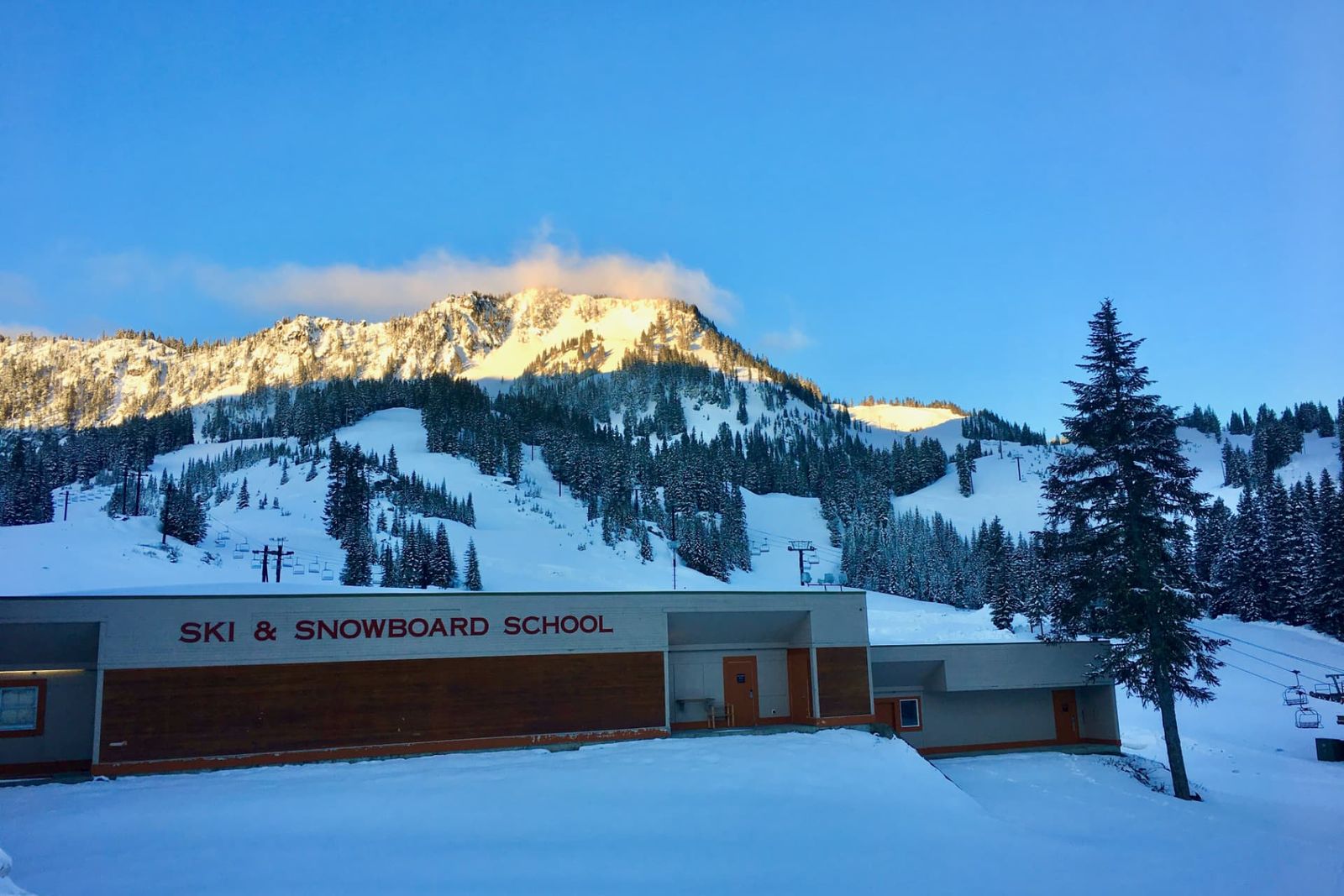 A mountain school building at dawn surrounded by snow and pine trees
