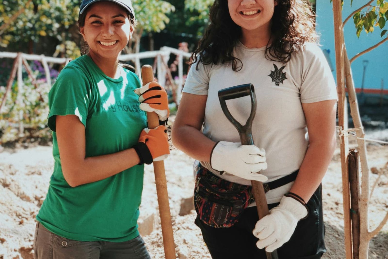 Two smiling volunteers holding shovels while planting a tree