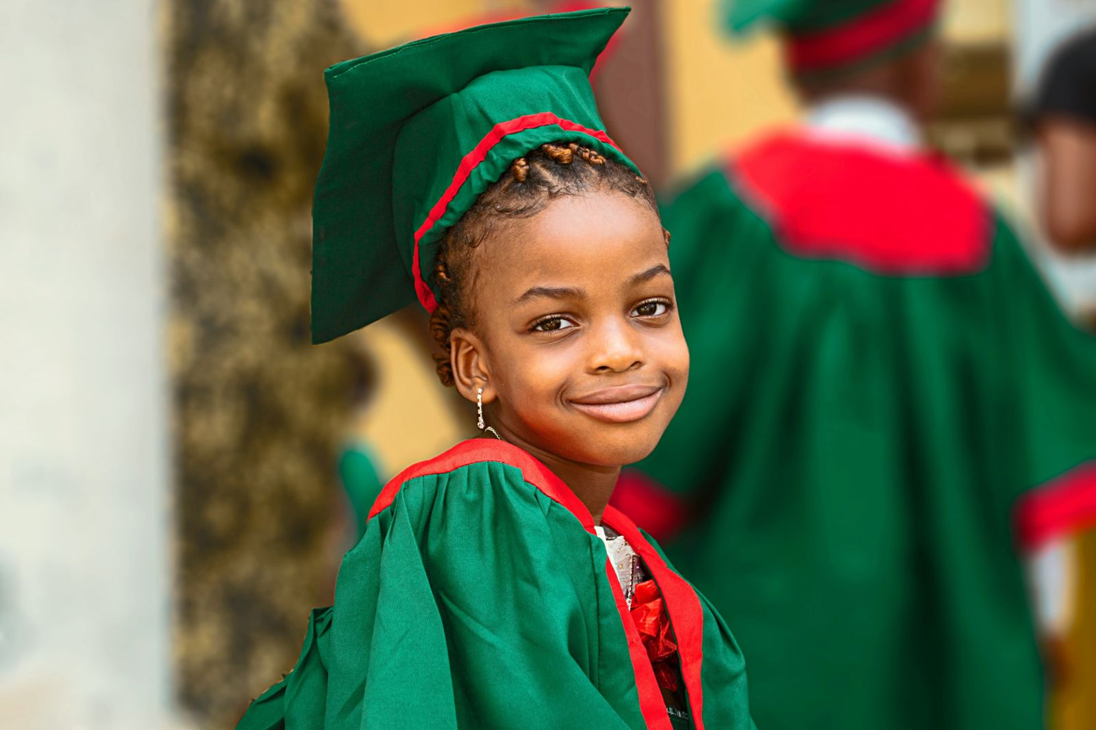 A young girl smiling in a green and red graduation cap and gown