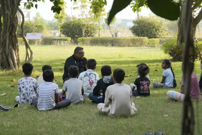 A teacher leading an outdoor lesson with children seated on the grass