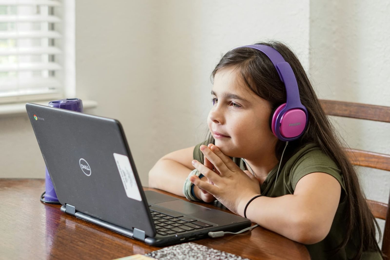 A young girl wearing headphones follows an online lesson on a laptop at home