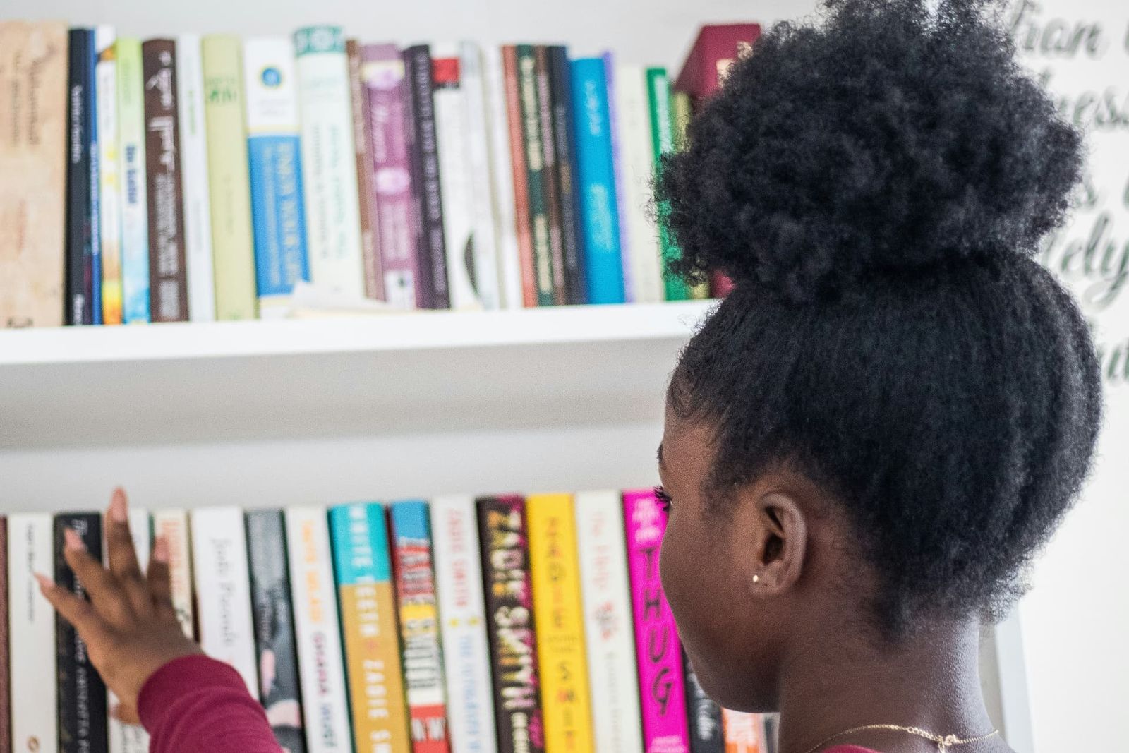 A girl choosing a book from a brightly coloured bookshelf