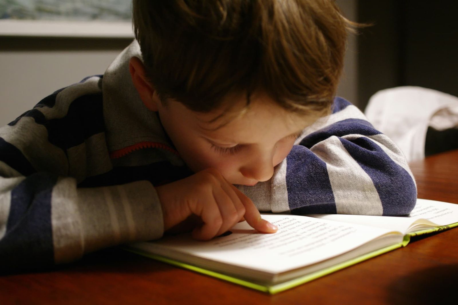 A young boy following the words with his finger while reading a book