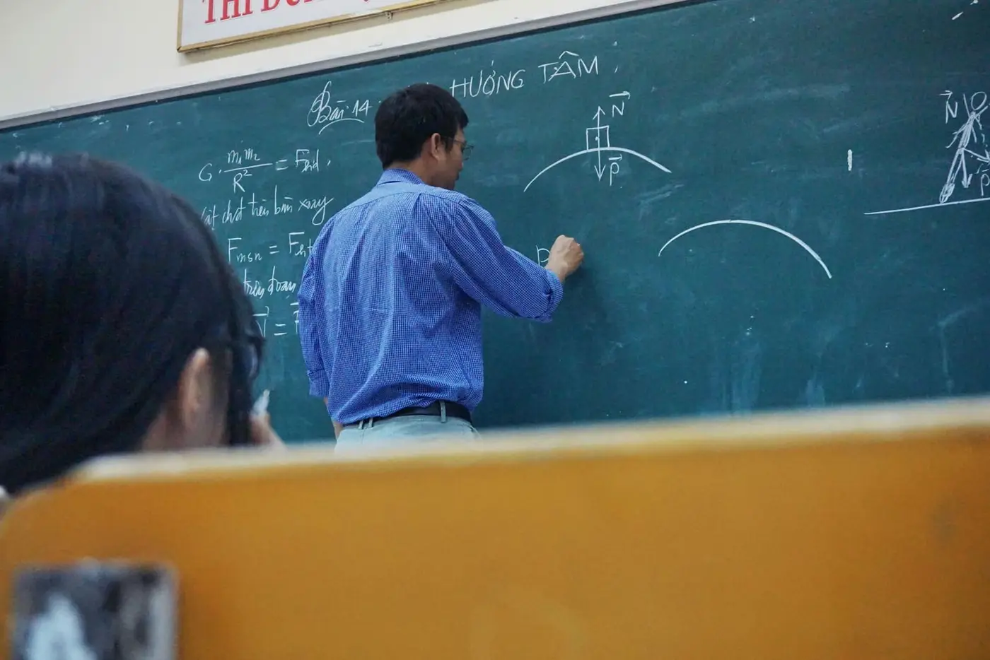 A teacher writing equations on a blackboard while pupils follow the lesson from their desks