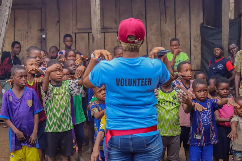 A volunteer leading a group of children in a warm-up activity outside a community centre