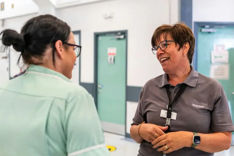 A volunteer in a badged polo shirt talking with a member of staff in a community facility