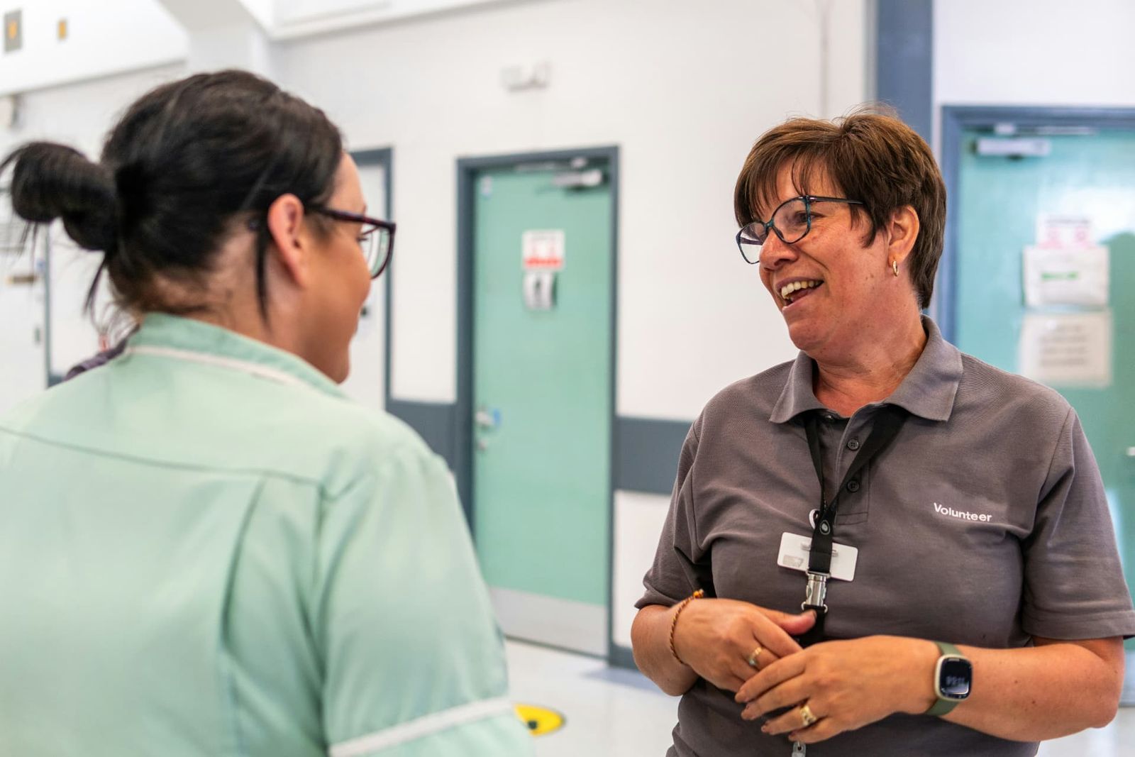 A smiling volunteer in a name badge talking with a member of staff